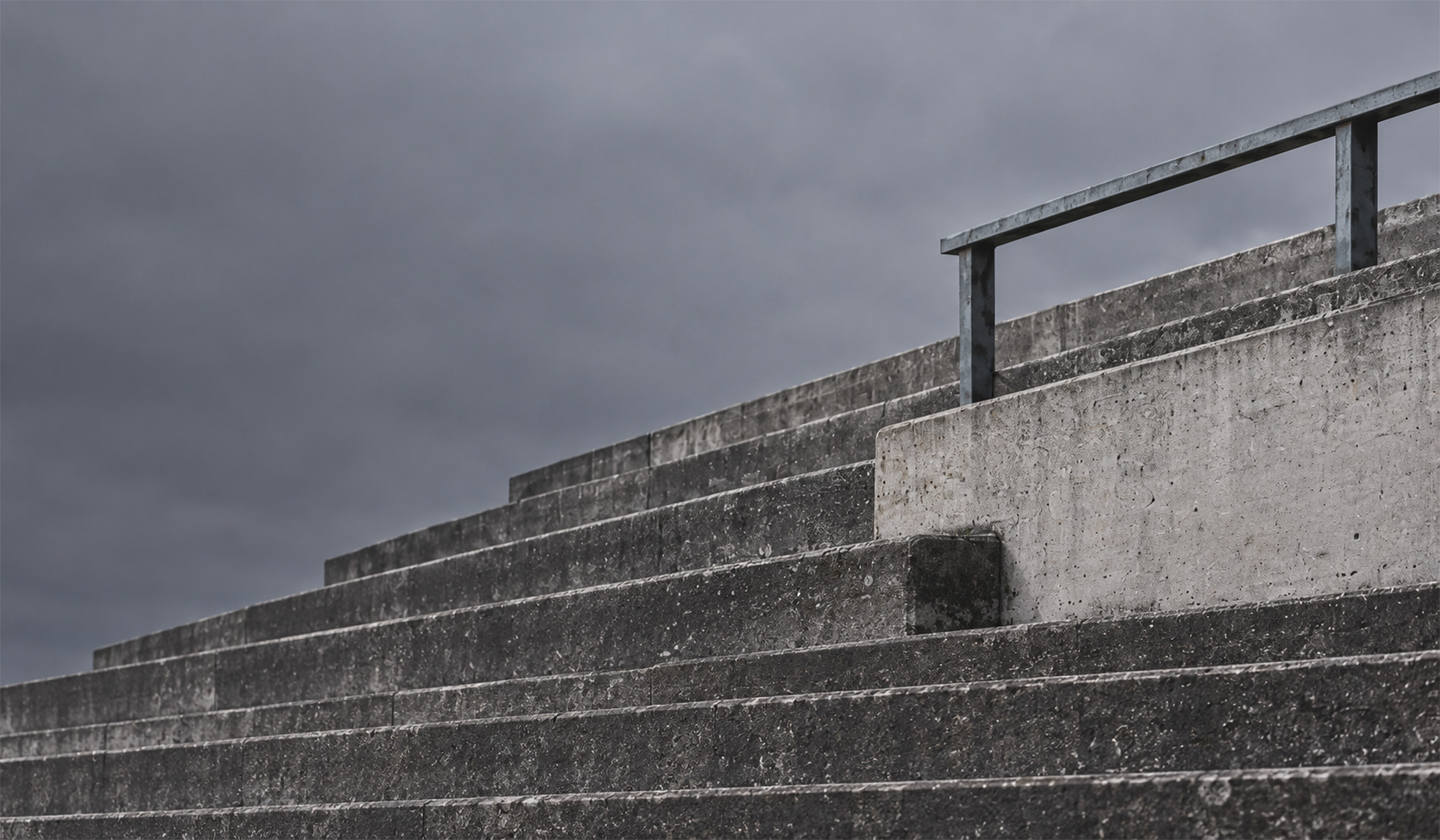 Empty concrete terrace steps at a football ground under an overcast sky.